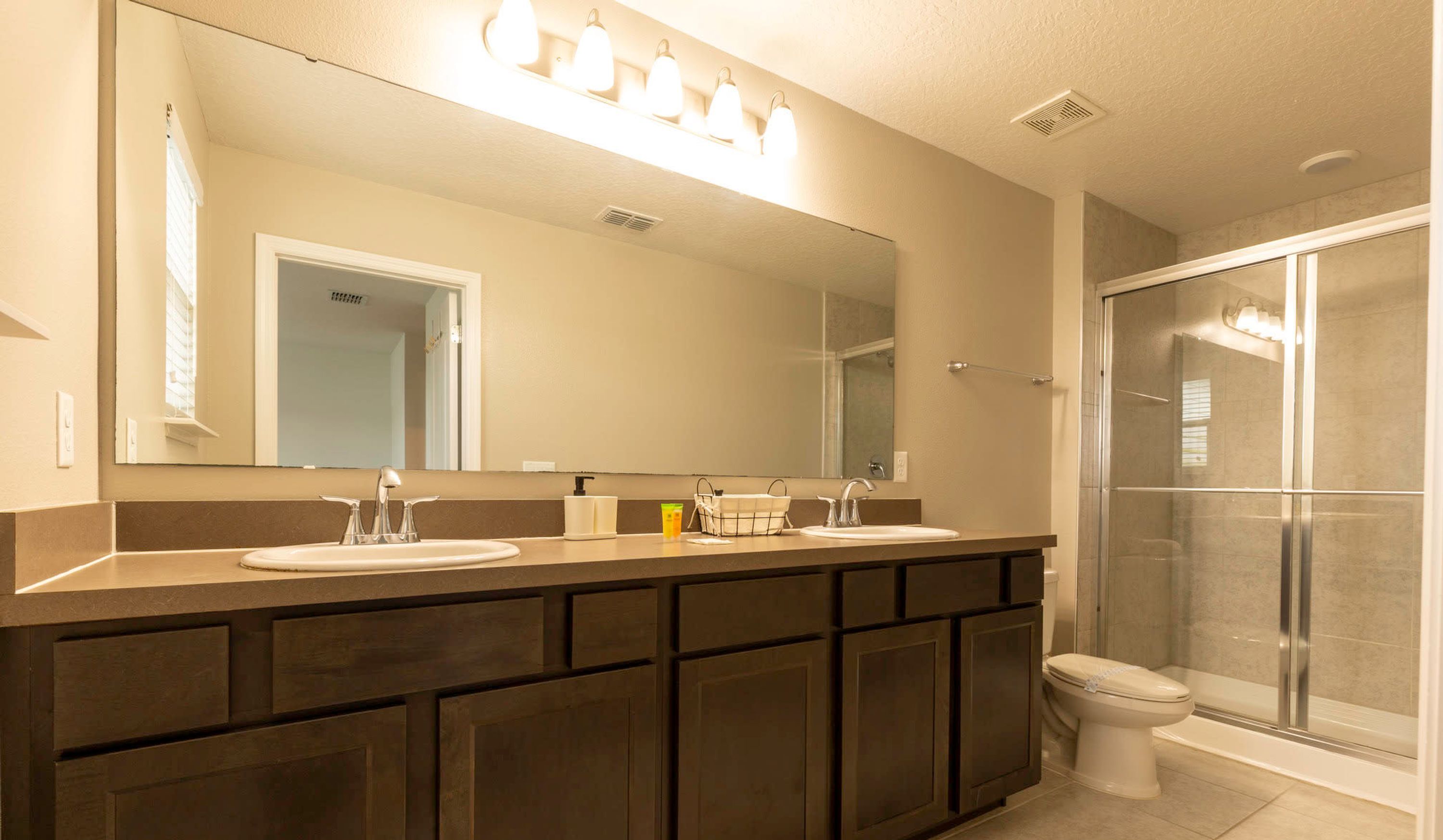 A bathroom with a double sink vanity, a large mirror, a shower enclosure, and a toilet.