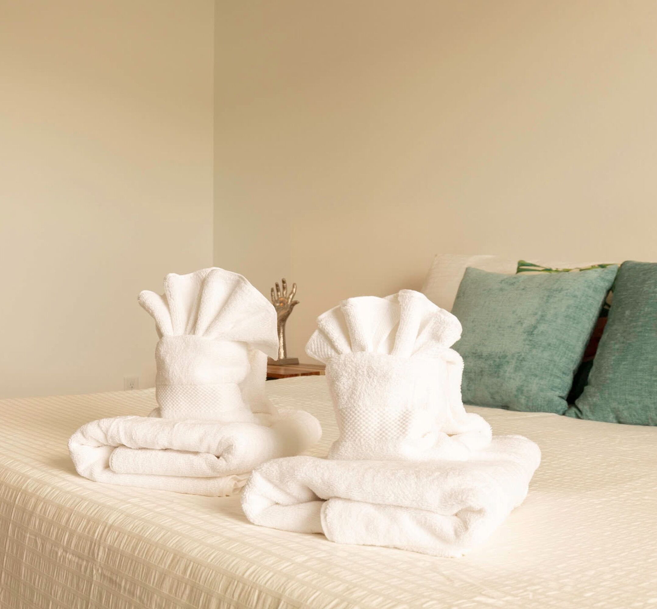 A neatly made bed with two folded white towels and a decorative hand-shaped object on a bedside table.