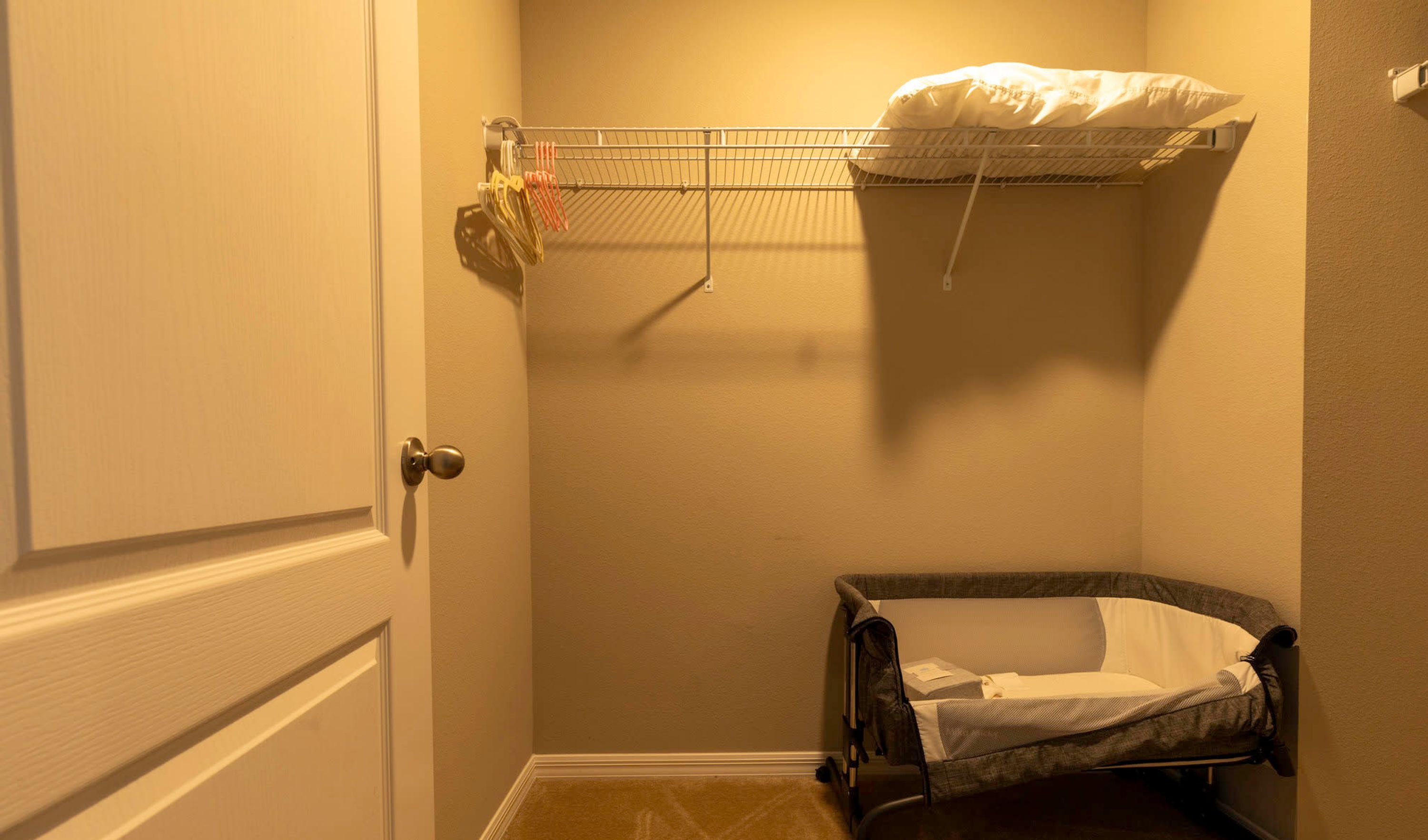 A small room with a door, a bunk bed with a mattress and pillows, and a crib with a blanket.