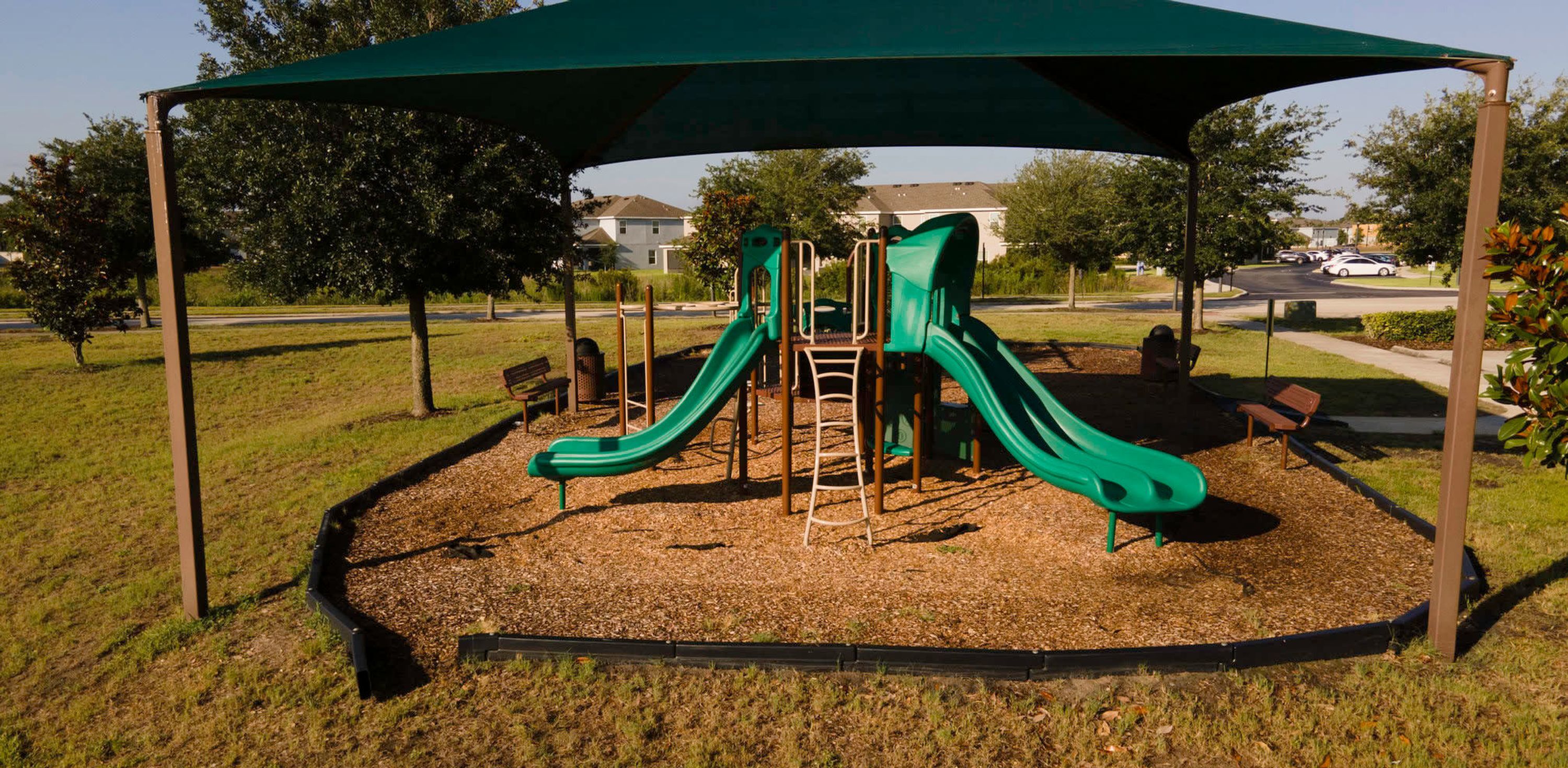 A playground with two slides and a climbing structure, surrounded by a covered area and benches.