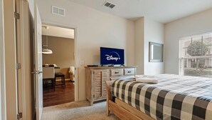A hotel room with a bed, a desk with a chair, a television displaying the Disney+ logo, and a window with blinds. - Family Spacious 3BR Townhouse With Pool Access (Kissimmee)