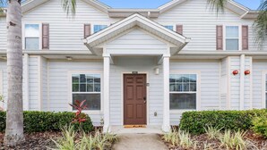 A two-story house with a brown front door, white siding, and a small porch. - Family Spacious 3BR Townhouse With Pool Access (Kissimmee)