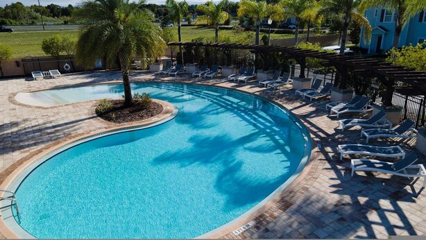 A large, curved swimming pool with lounge chairs and a pergola. - Family Spacious 3BR Townhouse With Pool Access (Kissimmee)