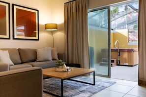 Un salon moderne avec un canapé, une table basse et une lampe. Une porte-fenêtre coulissante donne accès à un balcon équipé d’un jacuzzi.