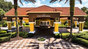 A hotel entrance with a red-tiled roof, yellow columns, and a checkered pathway leading to the doors. - Townhome Jacuzzi Grill 10 min Disney (Kissimmee)