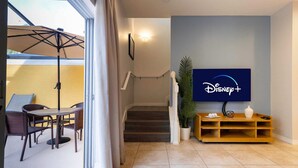 A living room with a TV displaying the Disney+ logo, a staircase, and a dining area with chairs and a table. - Townhome Jacuzzi Grill 10 min Disney (Kissimmee)