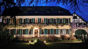 A two-story building with green shutters, a central entrance, and a garden with pink flowers. - Gutshause Suite #1 "elisabeth" im Weingut Fitz-ritter - Vdp/biozertifiziert (Bad Dürkheim)