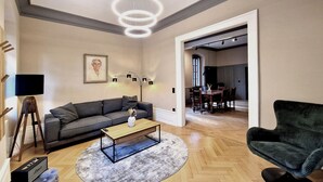 A modern living room with a sofa, a coffee table, and a dark armchair. There is a dining area visible through an open doorway. - Gutshause Suite #1 "elisabeth" im Weingut Fitz-ritter - Vdp/biozertifiziert (Bad Dürkheim)
