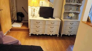 Une chambre à coucher comprenant un lit, une commode avec un miroir, une télévision et une étagère avec des objets décoratifs.