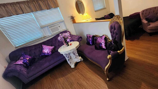 Une pièce avec un canapé violet, un fauteuil assorti, une petite table ronde et un miroir décoratif.