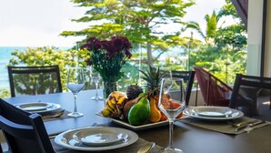 A table set for a meal with tropical fruits, a vase of flowers, and a view of the ocean. - Beach and Mountain by Horizon Holidays (Black River)