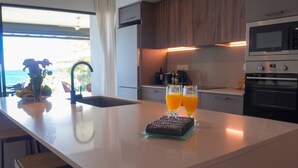 A modern kitchen with a view of the ocean, a sink, and two glasses of orange juice on a glass tray. - Beach and Mountain by Horizon Holidays (Black River)