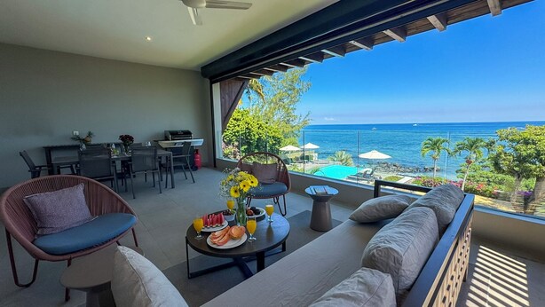 A balcony with a view of the ocean, a dining area, and a seating area with a table set for breakfast. - Beach and Mountain by Horizon Holidays (Black River)