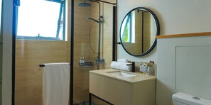 Une salle de bain avec une douche à parois de verre, un miroir rond, un lavabo avec des articles de toilette et un porte-serviettes.