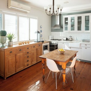 A kitchen with wooden cabinets, a central island with a bowl of fruit, a dining table with chairs, and a modern stove. - De Waterkant Guest Suites (Cape Town)