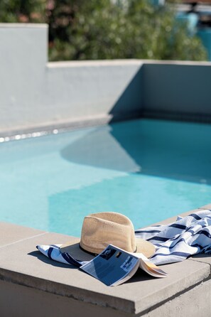 A poolside area with a concrete edge, a hat, and a striped towel. - De Waterkant Guest Suites (Cape Town)