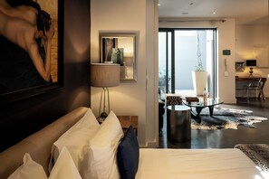 Una camera d'albergo moderna con un letto grande, un'area salotto con un tavolino in vetro e vista sulla città dal balcone.