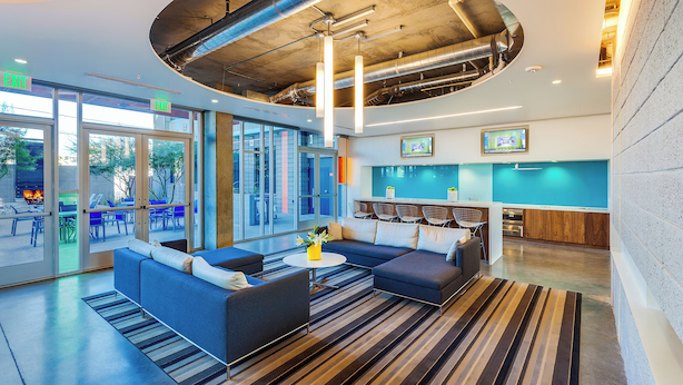 A modern lobby with a seating area, a kitchen, and a large window overlooking the outdoors. - Roosevelt Point (Phoenix)