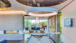 A pool table in a modern lounge area with a fireplace, seating, and a large screen. - Roosevelt Point (Phoenix)
