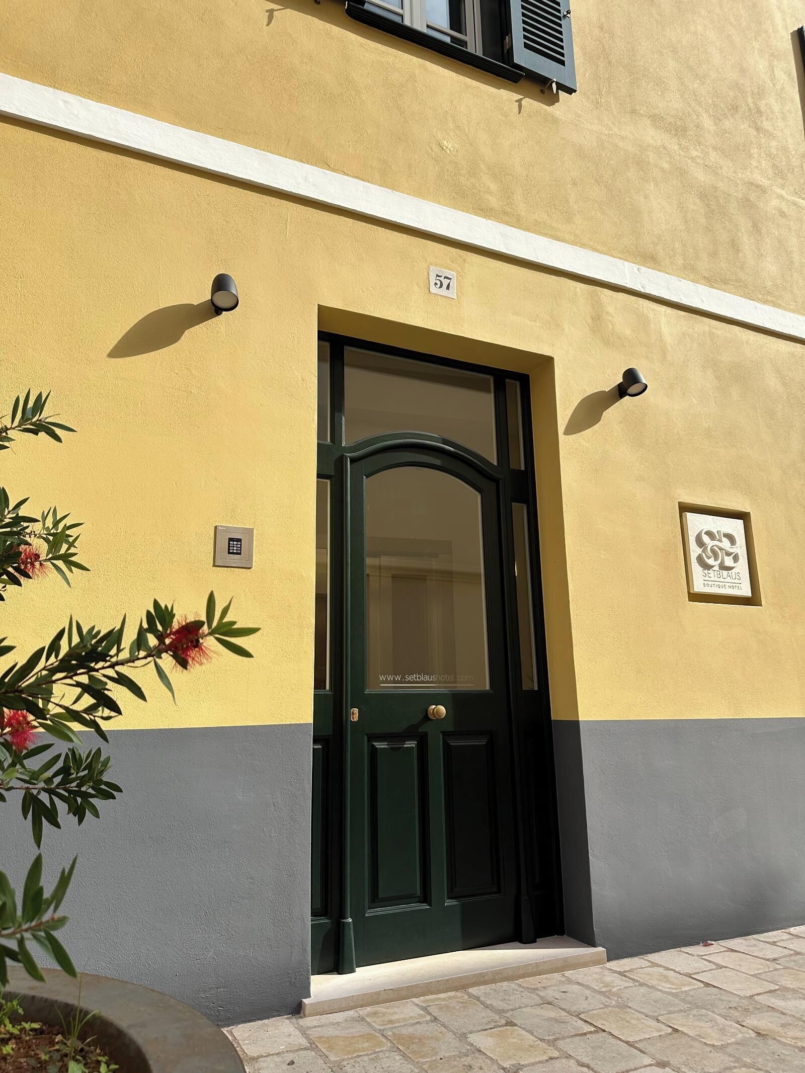 Ein Gebäude mit grüner Tür, einem Schild mit der Aufschrift 57 und einem kleinen Fenster mit einer Lampe.