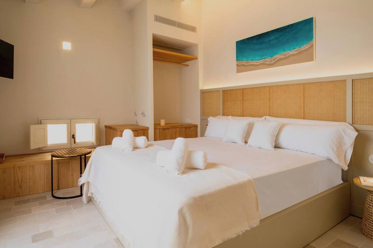 A hotel room with a large bed, a wooden nightstand, a small table, a mirror, and a wall-mounted artwork.