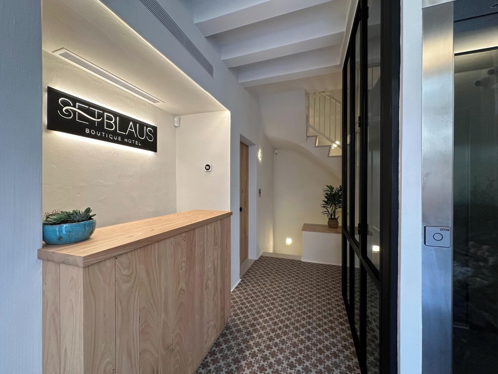 A hotel reception area with a wooden reception desk, a sign reading "SEEBLAUS BOUTIQUE HOTEL", and a patterned floor.