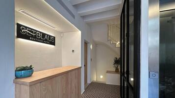 A hotel reception area with a wooden reception desk, a sign reading "SEEBLAUS BOUTIQUE HOTEL", and a patterned floor.