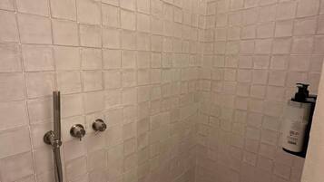 Ein kleiner Duschbereich mit Fliesen, einer Handbrause und einem am Wand montierten Wasserhahn.