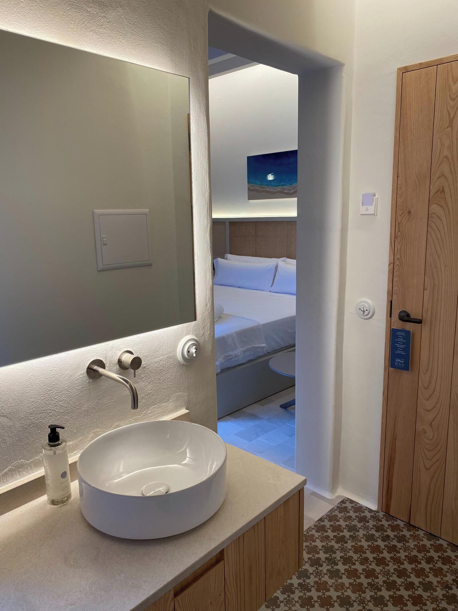 A bathroom with a round sink, a mirror, and a hand soap dispenser.