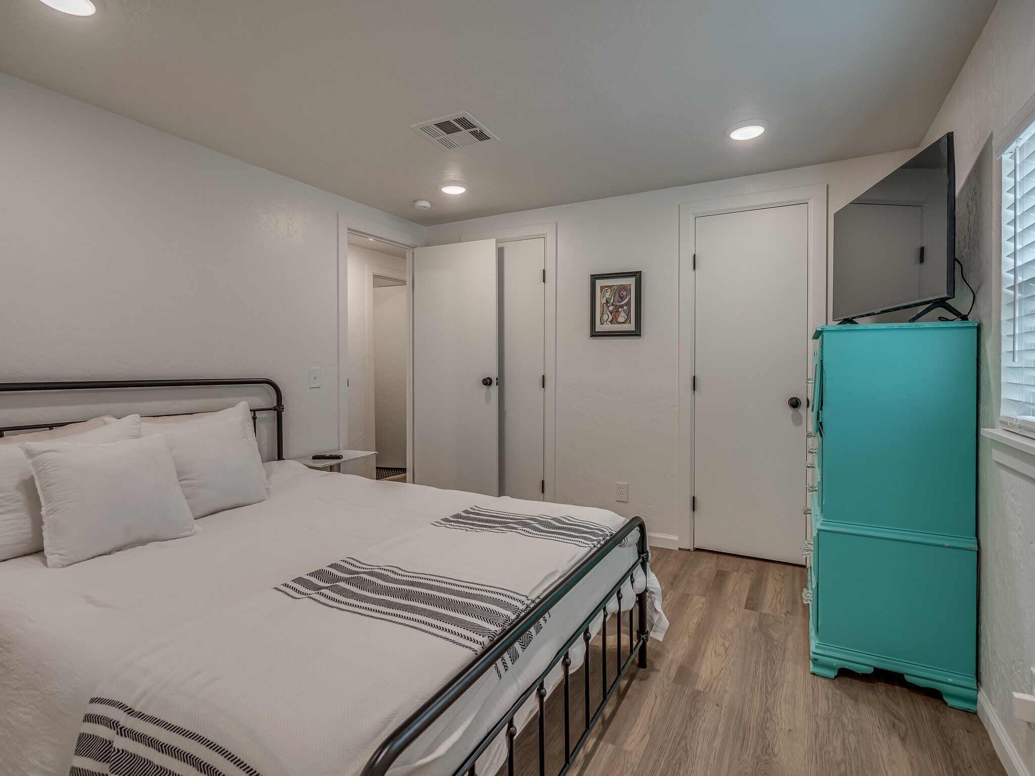 Ein Schlafzimmer mit einem Bett, einer türkisblauen Kommode, einer Tür und einem kleinen Tisch.