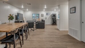 Una cuina moderna amb forn integrat, zona de menjador amb taula i cadires de fusta, i saló amb sofà i televisió.