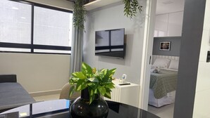 Une chambre d’hôtel moderne avec une table en verre, une plante en pot, un lit recouvert d’une couverture verte et un téléviseur fixé au mur.
