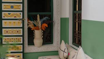 A room with a patterned wall, a window with decorative elements, a cushioned bench, and a wicker chair.