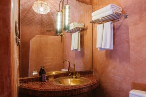 Un baño con lavamanos de azulejos, un espejo, un perchero para toallas y un inodoro.