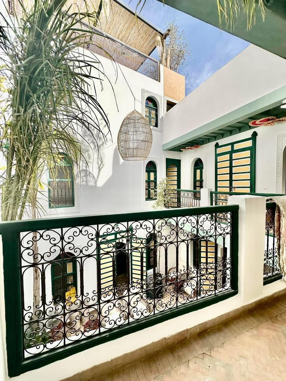 Un edificio blanco con contraventanas verdes, una cerca metálica decorativa y una palmera.
