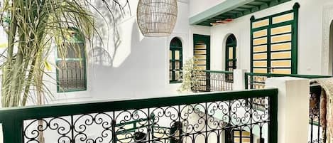 Un edificio blanco con contraventanas verdes, una cerca metálica decorativa y una palmera.