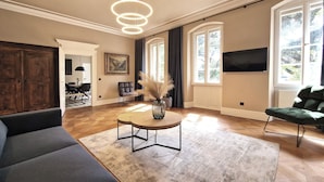 A spacious living room with a large sofa, a round coffee table with a vase, and a television on the wall. - Gutshaus Suite #2 "magdalena" im Weingut Fitz-ritter - Vdp/biozertifiziert (Bad Dürkheim)