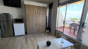 Una cocina moderna con horno empotrado, microondas y cafetera. Hay una zona de comedor con mesa y sillas, y un balcón con vistas al puerto deportivo.