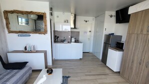 Un espacio habitable compacto con sofá, una mesa de centro, una zona de cocina con fregadero y estufa, y un televisor montado en la pared.