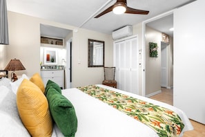 A bedroom with a bed, a ceiling fan, a white air conditioning unit, and a hallway leading to a closet. - Kona Alii#407: Corner Unit in the Heart of Kona! (Kailua-Kona)
