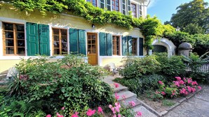 A yellow building with green shutters and a garden with pink flowers. - Gutshaus Suite #3 "emma" im Weingut Fitz-ritter - Vdp/biozertifiziert (Bad Dürkheim)
