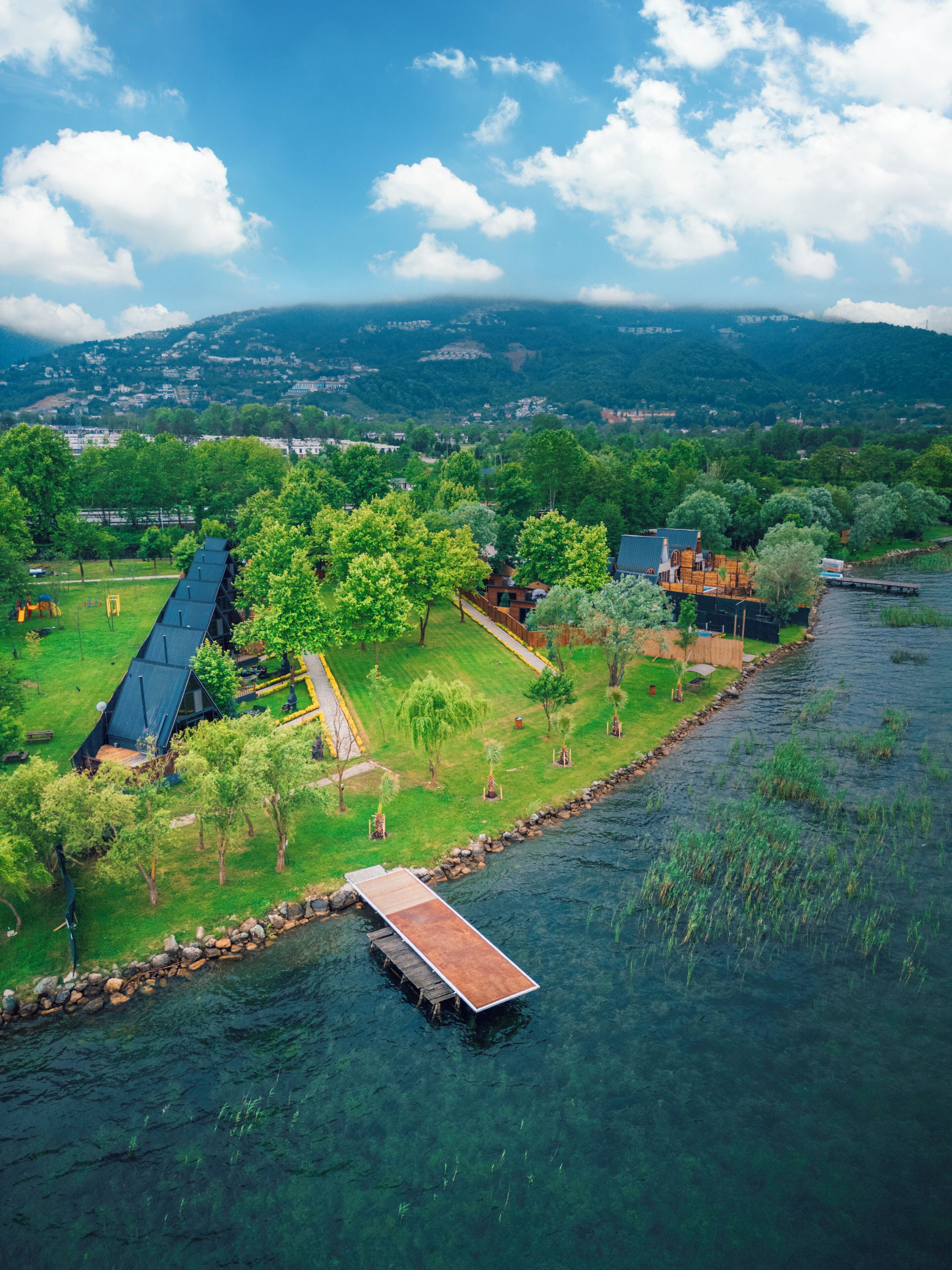 A riverside property with a wooden dock, a large house with a sloped roof, and a small cabin.