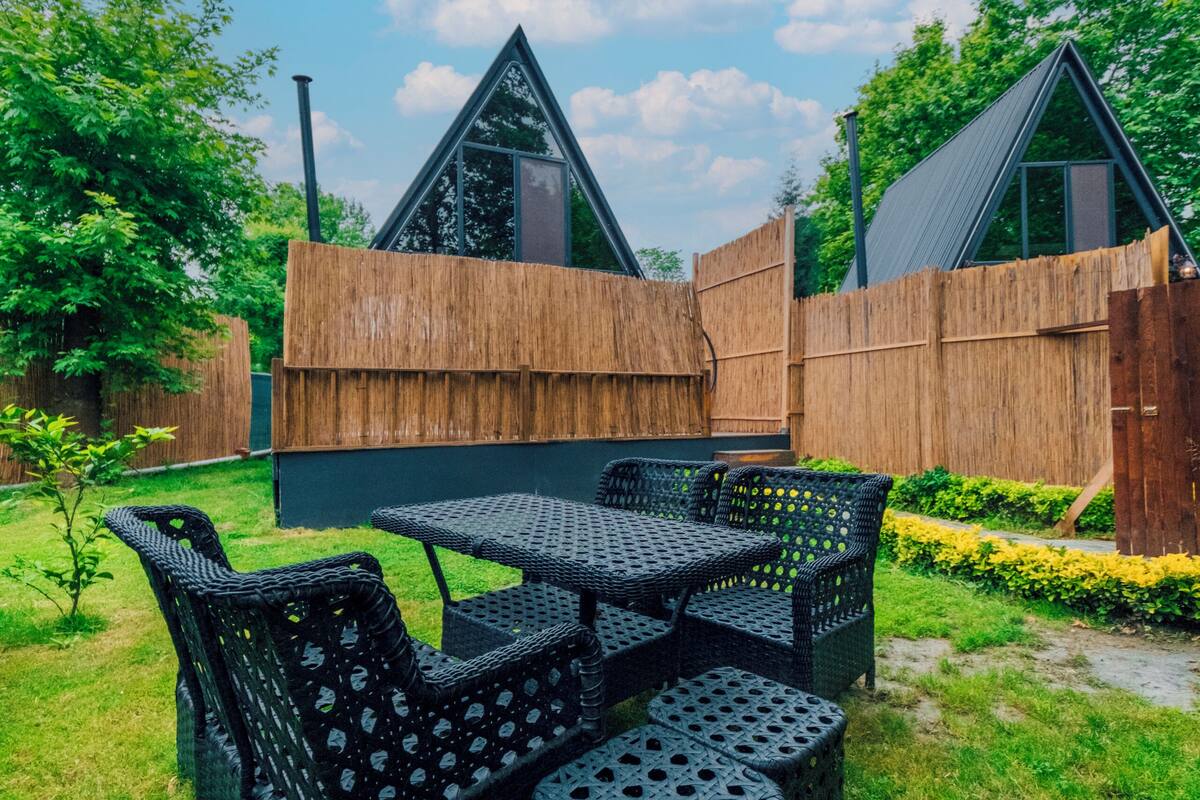 A backyard with a dining set, a wooden fence, and a thatched-roof structure.