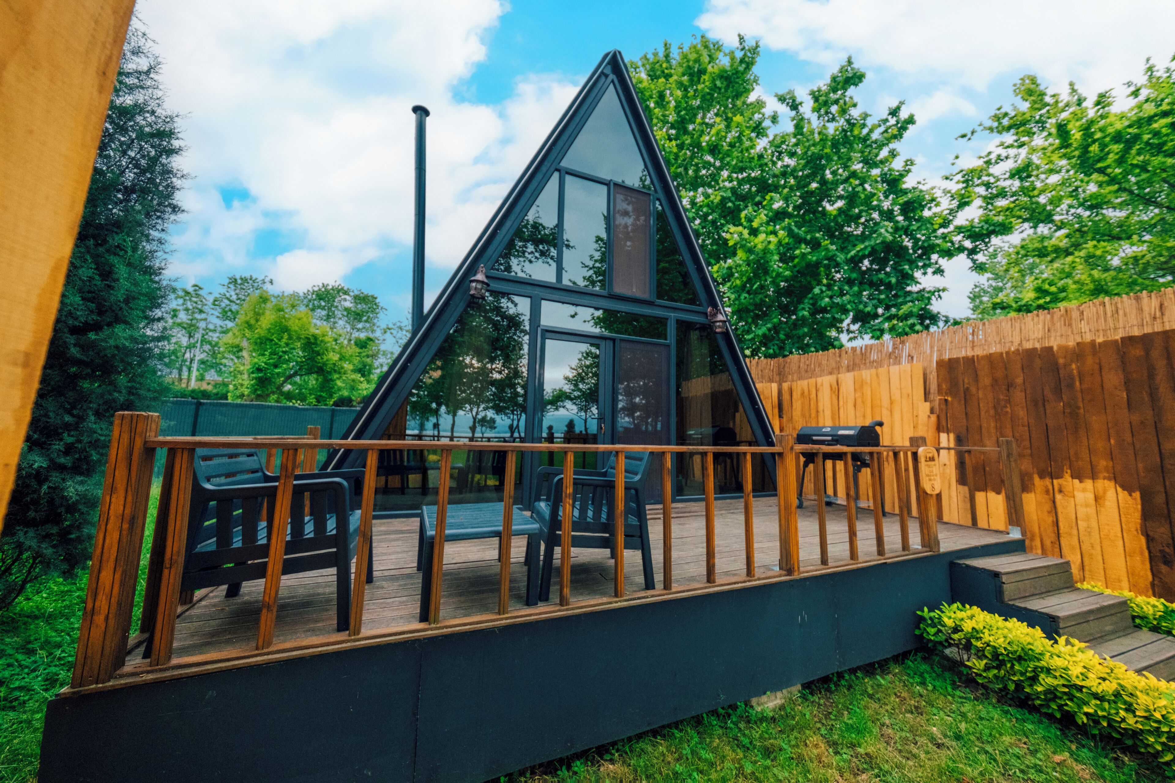 Una estructura con techo de cristal triangular, deck de madera y asientos al aire libre.