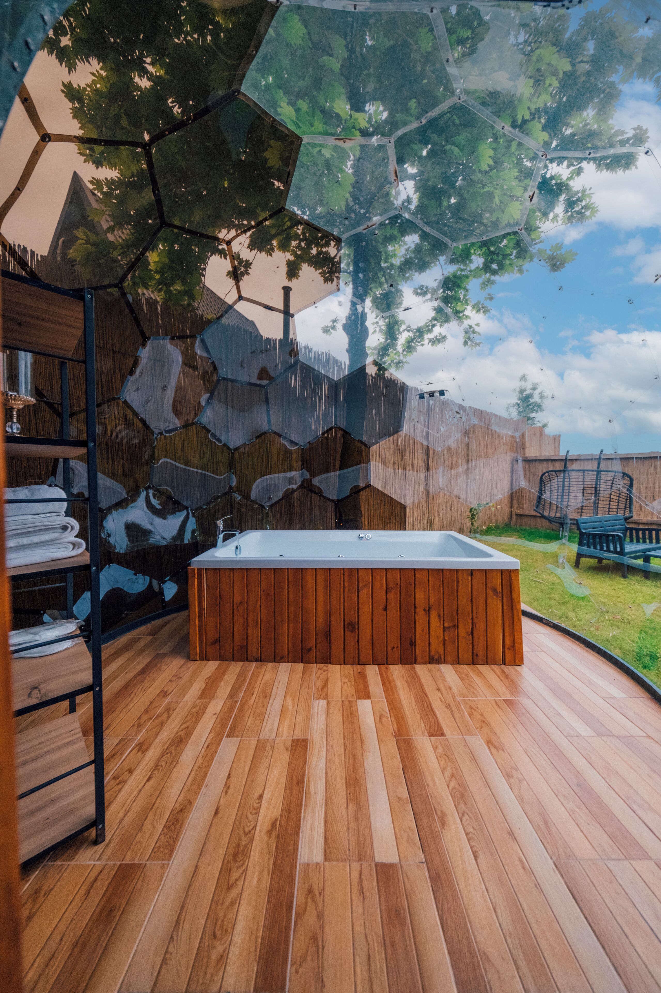 A wooden deck with a hot tub, a wooden shelf with towels, and a hexagonal wall design.