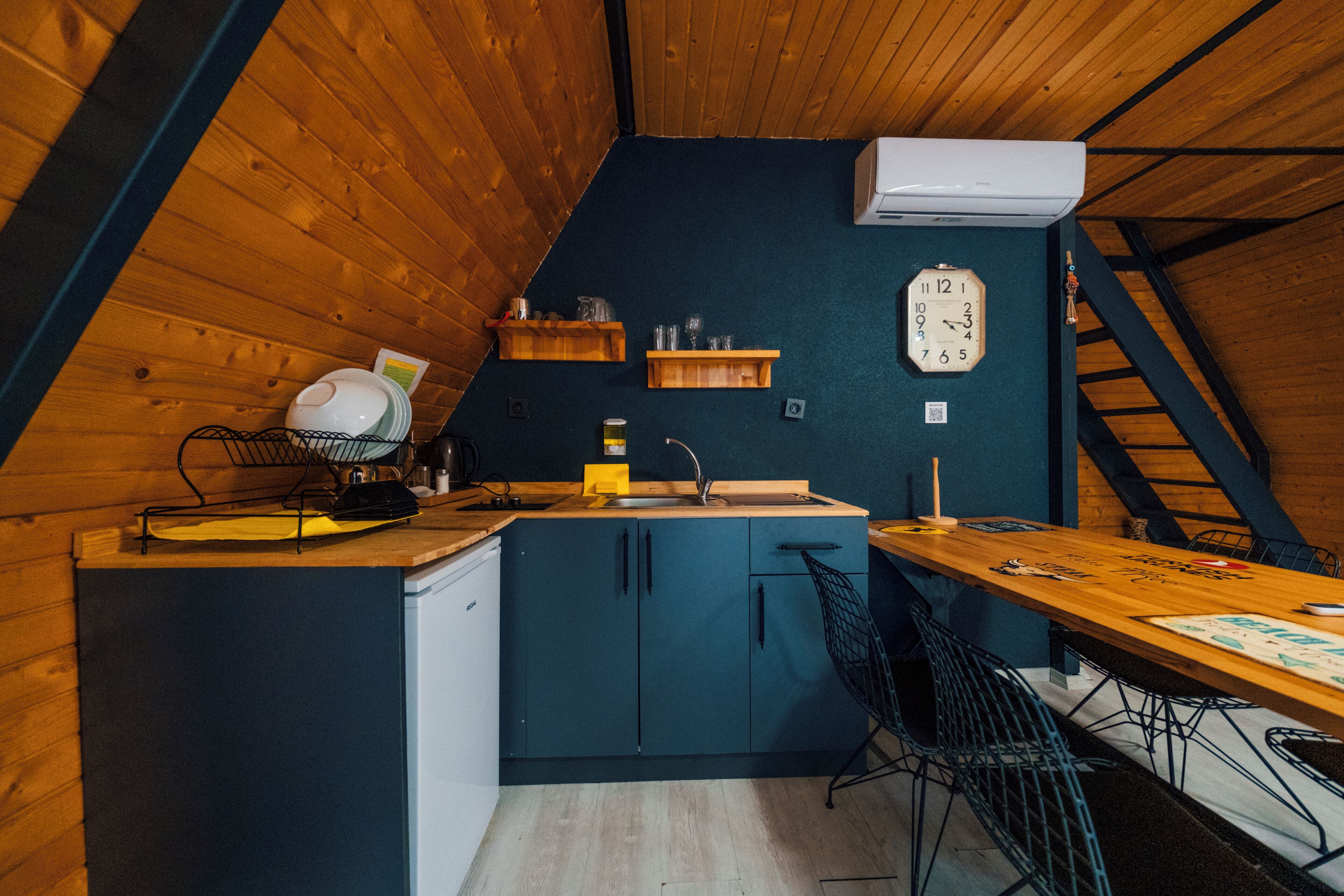 Une cuisine avec des meubles de rangement en bois, un évier et une horloge au mur.