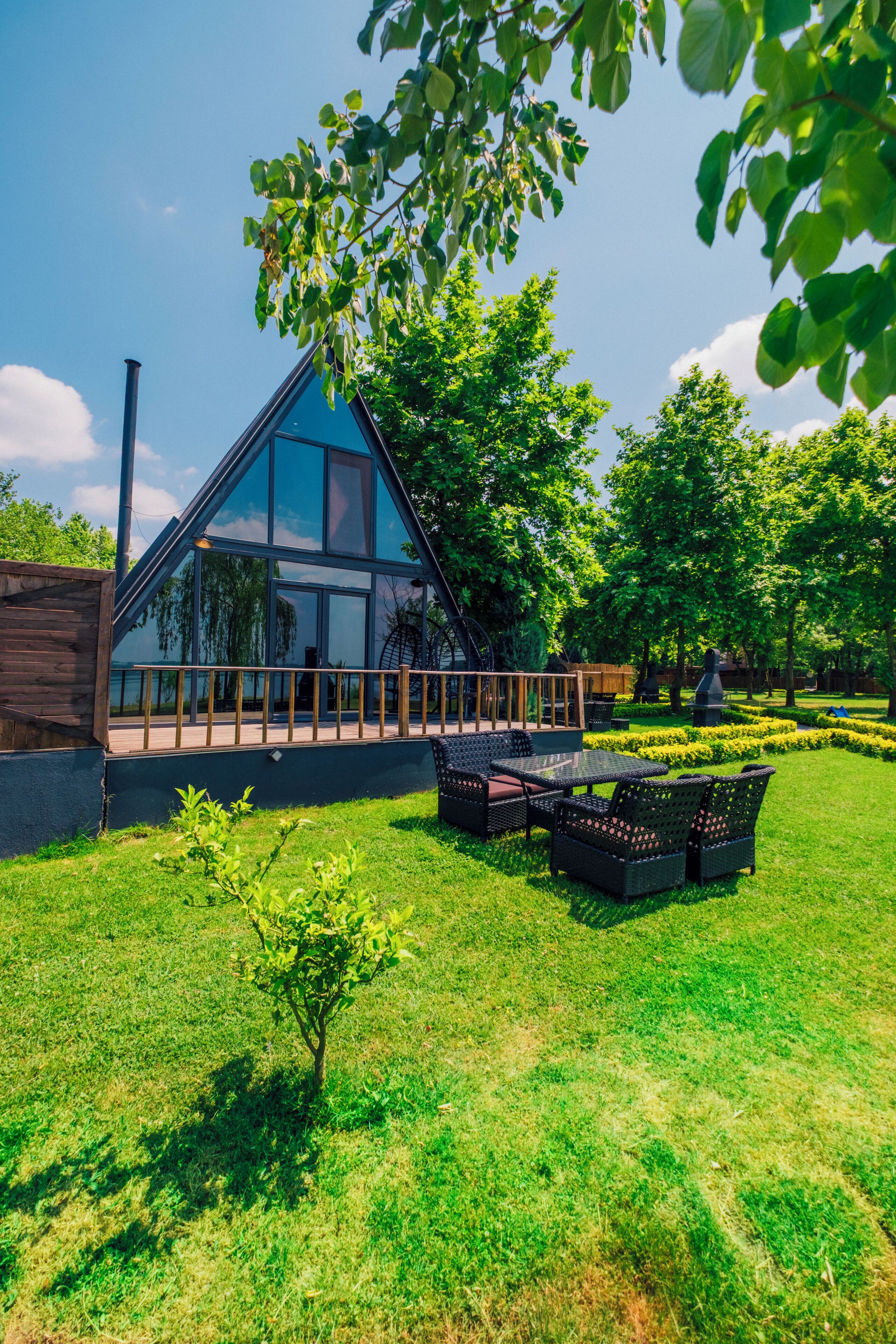 A modern glass house with a triangular roof, surrounded by a well-maintained lawn and trees.