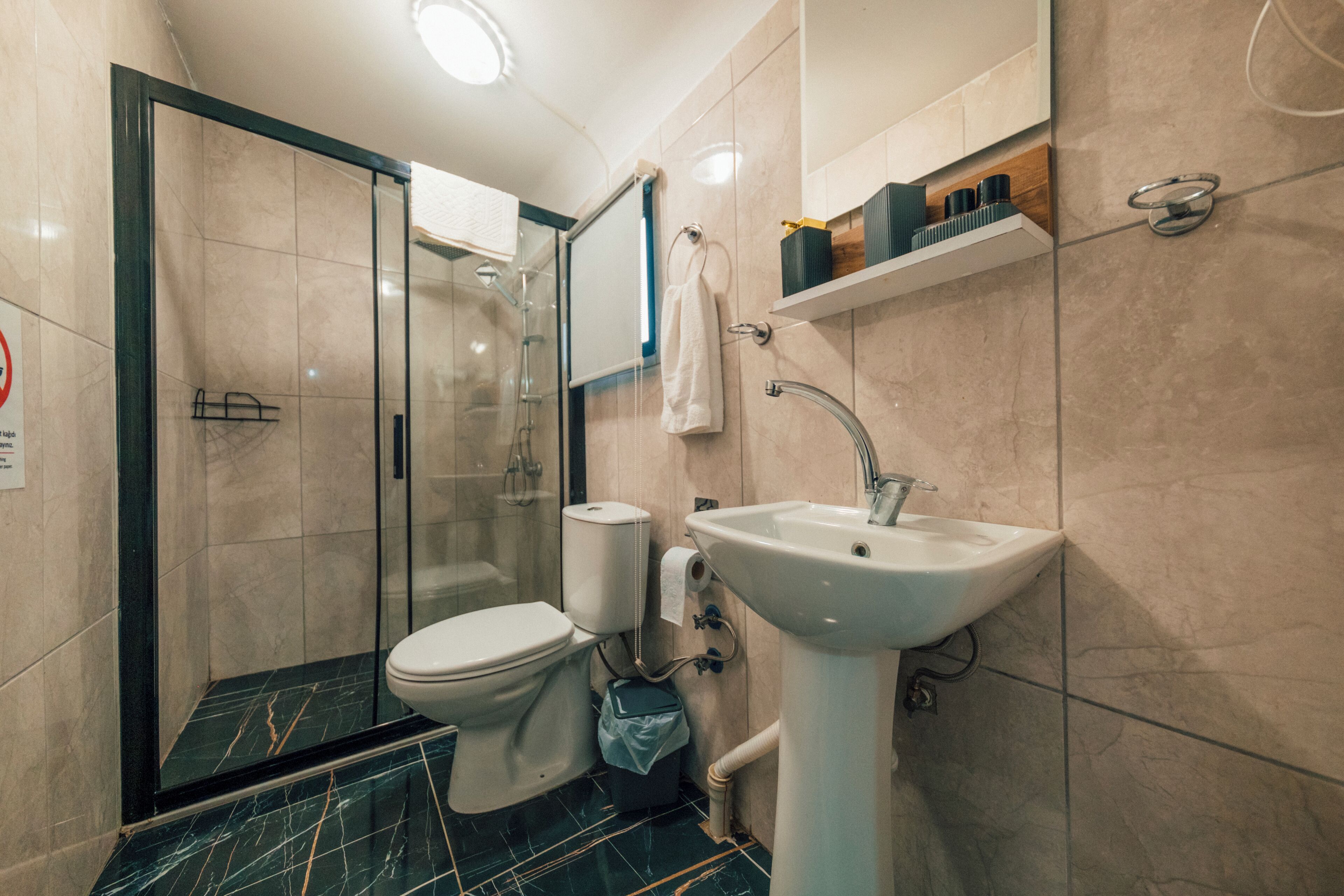 Un baño moderno con cabina de ducha de vidrio, inodoro blanco, lavamanos y una toalla colgada en la pared.