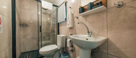 Un baño moderno con cabina de ducha de vidrio, inodoro blanco, lavamanos y una toalla colgada en la pared.