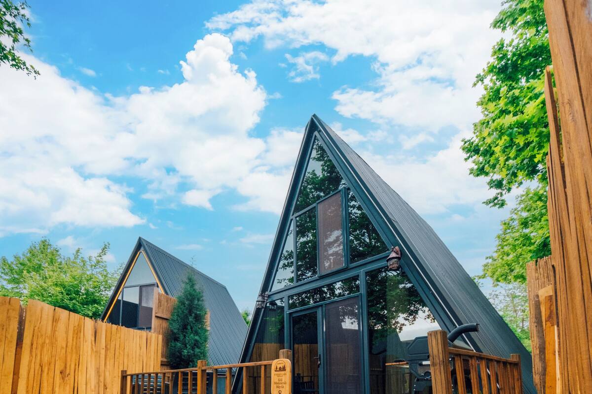 A modern house with a triangular roof, a wooden deck, and a paved pathway leading to the entrance.